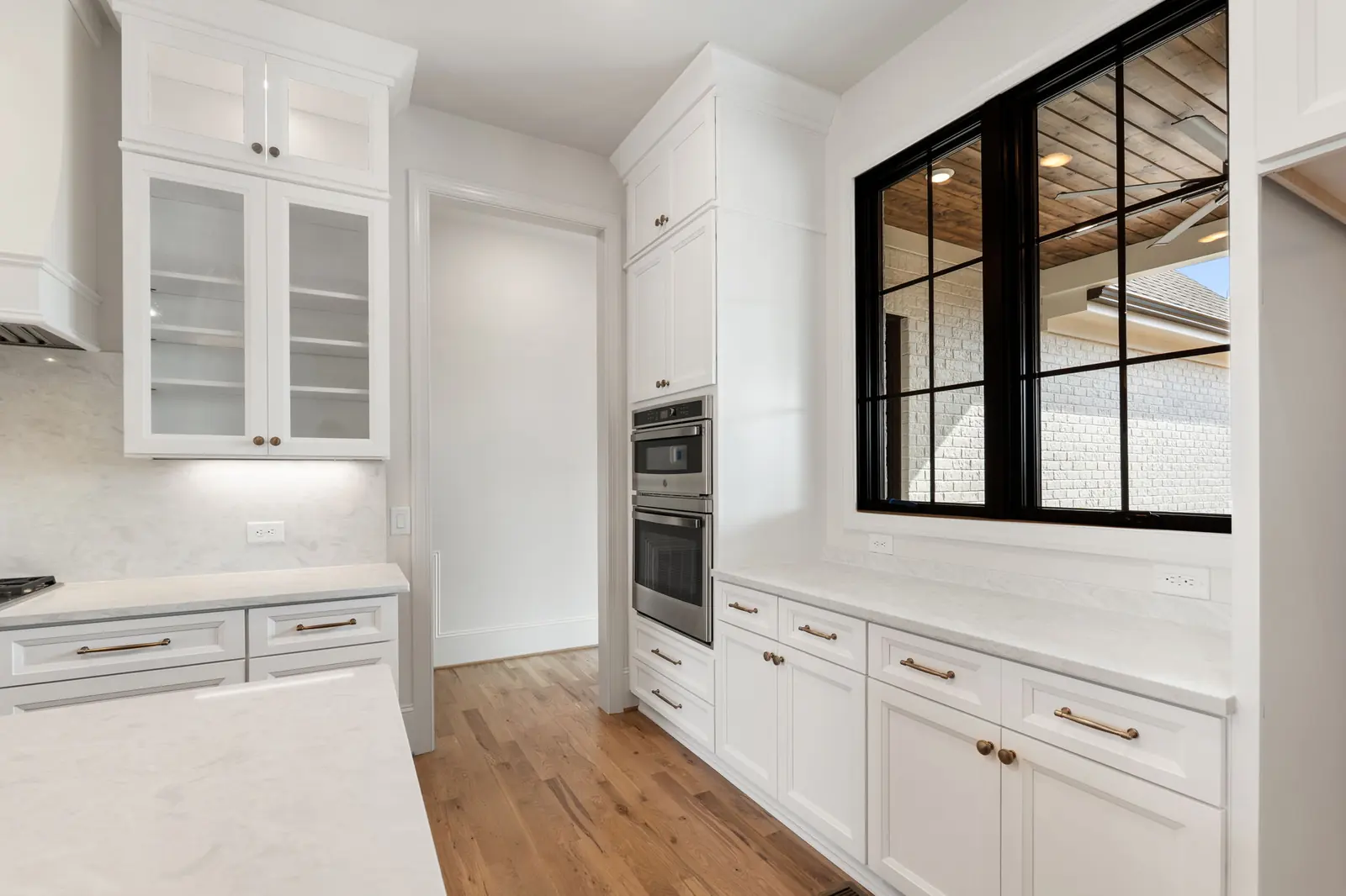White painted kitchen cabinetry with glass-front uppers and aged brass hardware