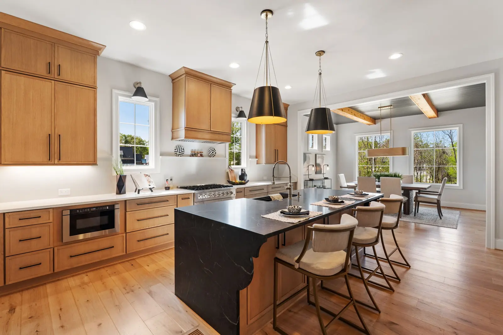 Kitchen island topped with honed black stone beside stained wood cabinetry